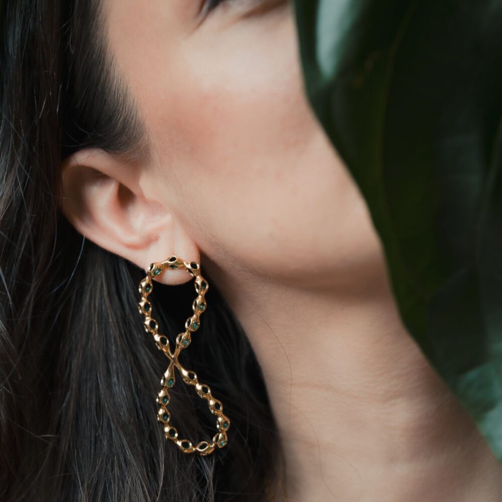 Close-up of Infinity large gold hoop earrings with turquoise stones, worn by a model with dark hair and natural makeup.