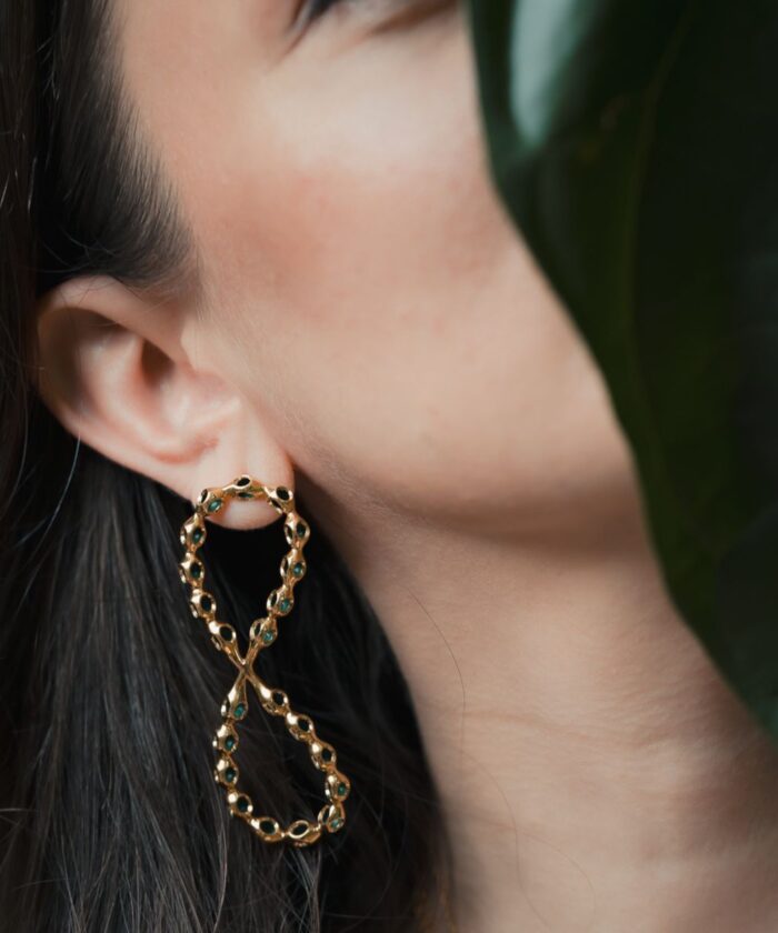 Close-up of Infinity large gold hoop earrings with turquoise stones, worn by a model with dark hair and natural makeup.