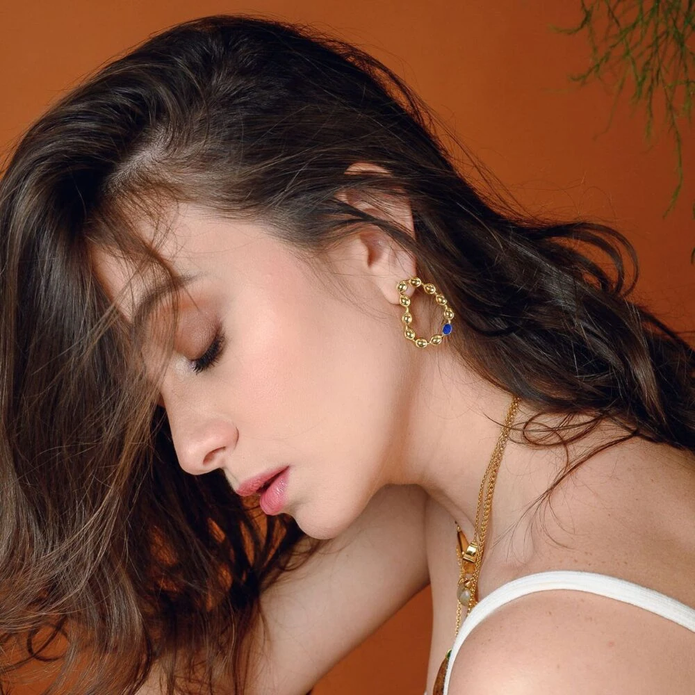 Close-up of a woman's face showcasing Monica Varela jewelry with a whimsical earring and elegant makeup.