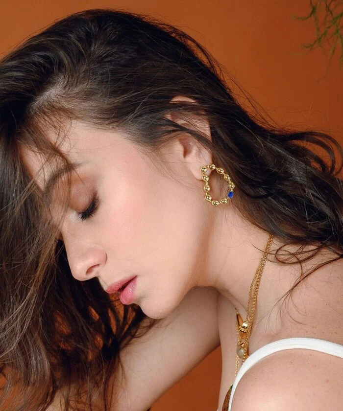 Close-up of a woman's face showcasing Monica Varela jewelry with a whimsical earring and elegant makeup.