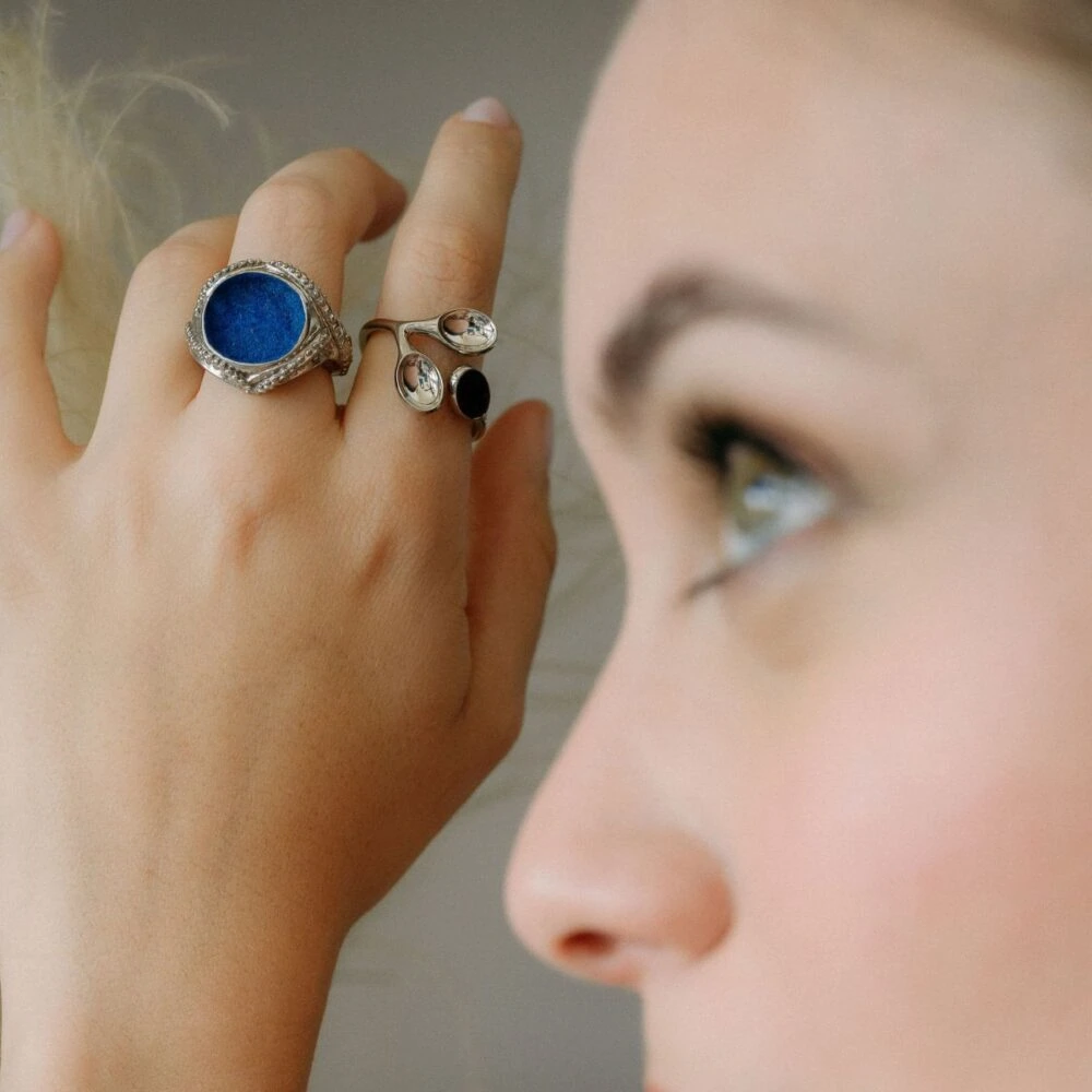 Close-up of stylish jewelry rings on woman's hand, featuring a blue gemstone ring and sleek silver designs.
