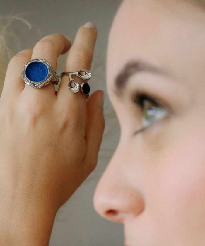 Close-up of stylish jewelry rings on woman's hand, featuring a blue gemstone ring and sleek silver designs.