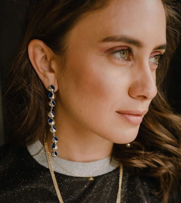 Close-up of Monica Varela wearing long dangle Trinity earrings and subtle makeup.