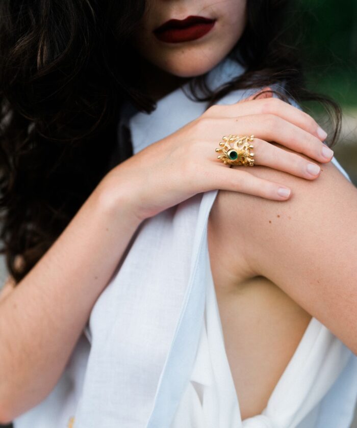 Close-up of woman wearing bold gold snake ring with green gemstone, emphasizing jewelry details.