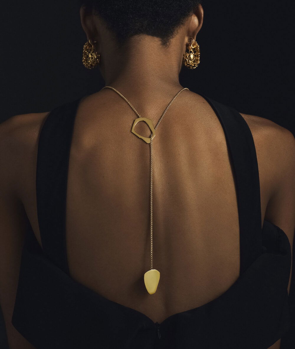 Gold lariat necklace with geometric pendant and dangling detail.