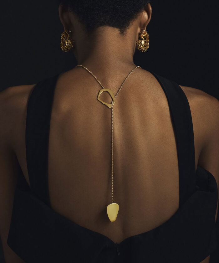 Gold lariat necklace with geometric pendant and dangling detail.