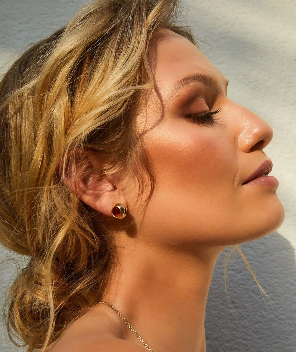 Close-up of Monica Varela wearing elegant small gold earrings.