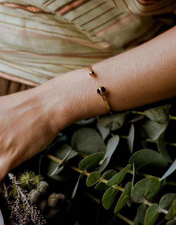 Delicate gold cuff bracelet featuring small red and black gemstones, perfect for elegant accessorizing.