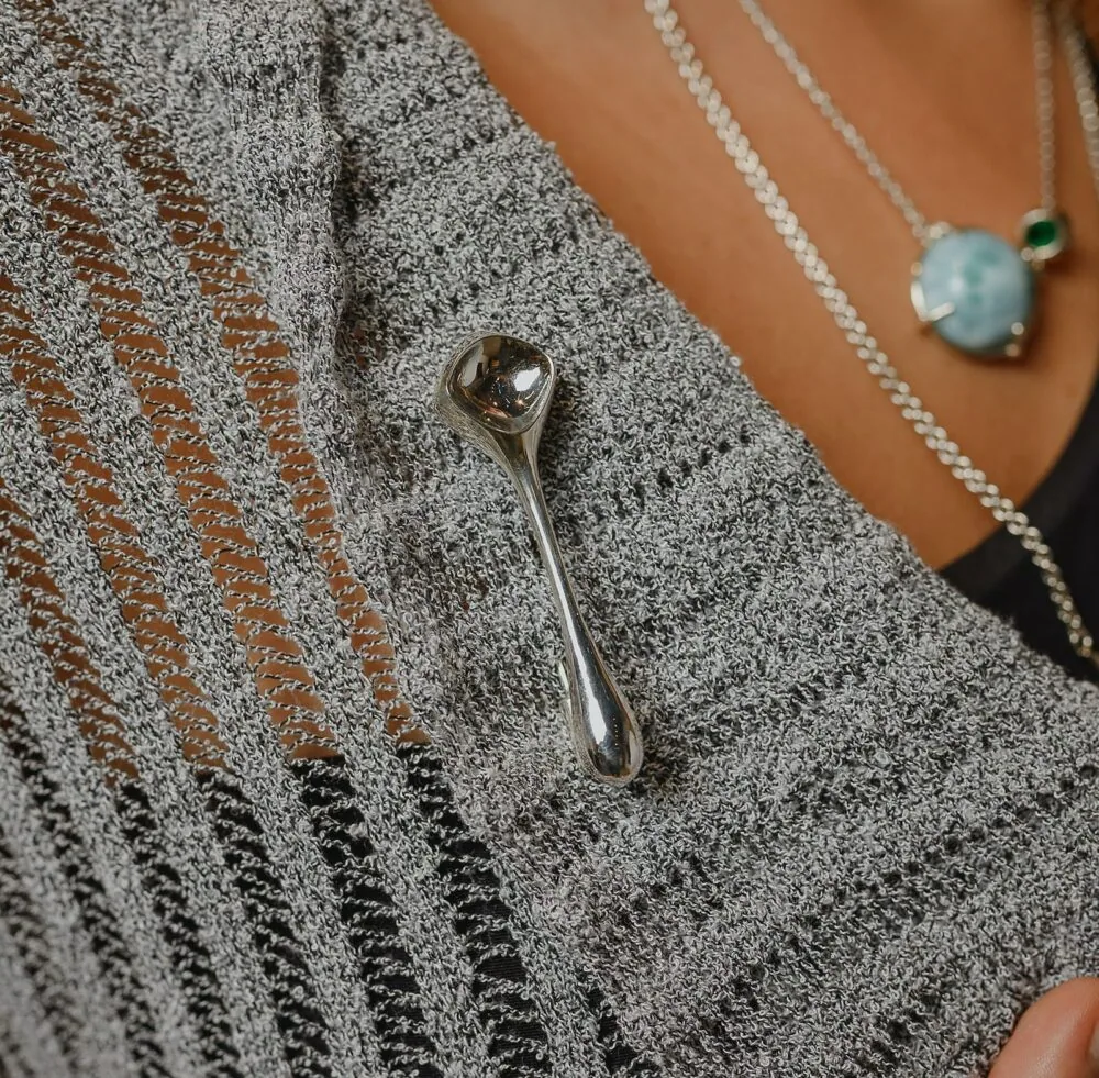 Close-up of a silver decorative pin attached on a knitted grey sweater with textured needlework.