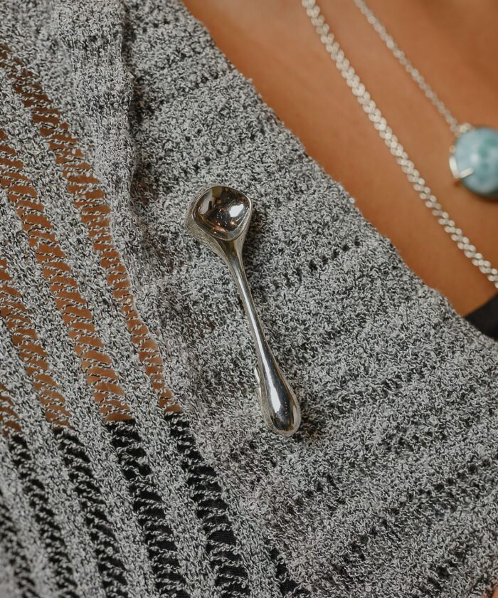 Close-up of a silver decorative pin attached on a knitted grey sweater with textured needlework.