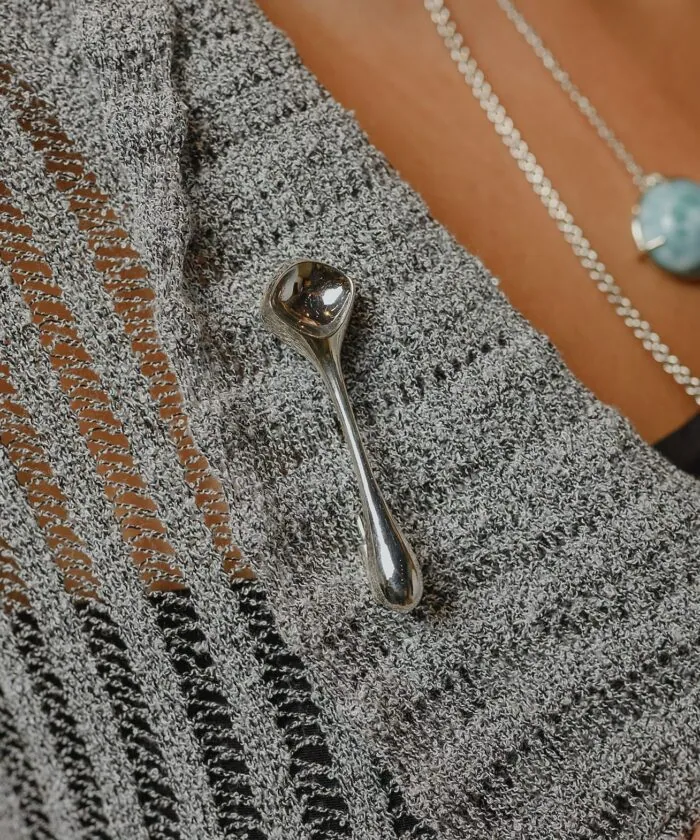 Close-up of a silver decorative pin attached on a knitted grey sweater with textured needlework.