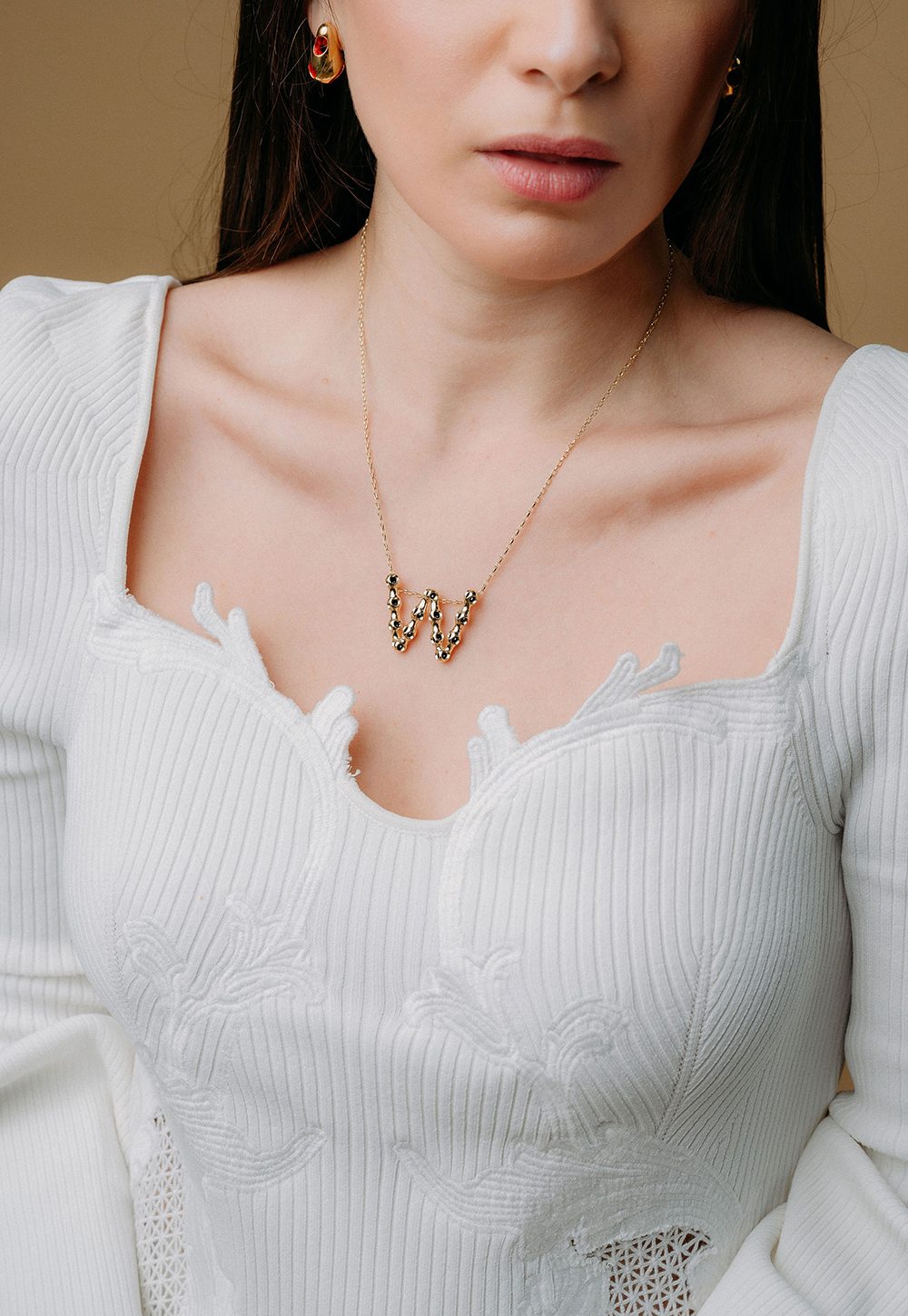 Monica Varela necklace Close-up of Monica Varela jewelry with a "W" pendant on a woman’s neck.