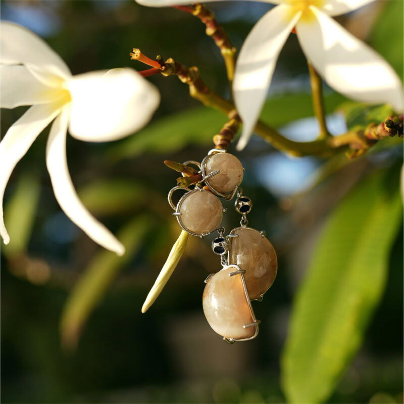 Close-up of beige gemstone jewelry hanging from a flowering tree branch with white blossoms.